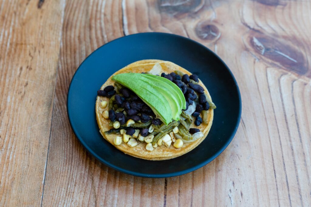 Delicious Mexican tostada with avocado, black beans, and corn on a rustic wooden table.