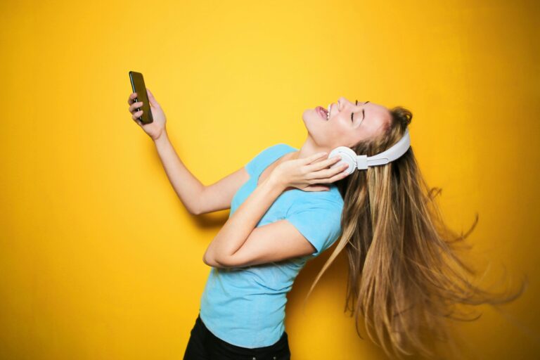 Joyful young woman enjoying music with headphones against a yellow background.