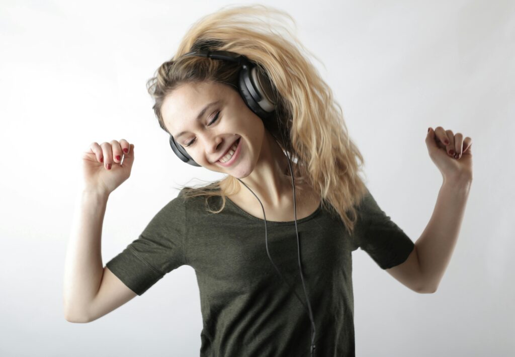 A happy woman with blonde hair dances joyfully while listening to music on headphones.