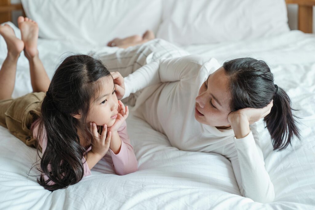 A mother and daughter bonding indoors, lying on a bed and enjoying quality time together.