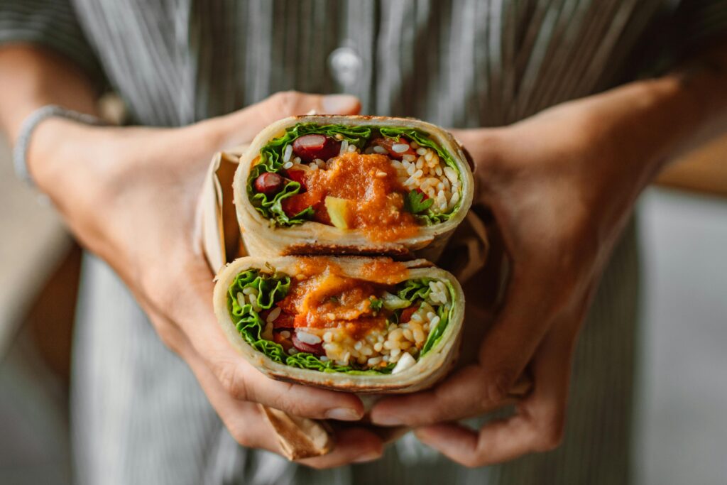 Close-up of hands holding a fresh vegetable wrap filled with colorful ingredients and sauce.
