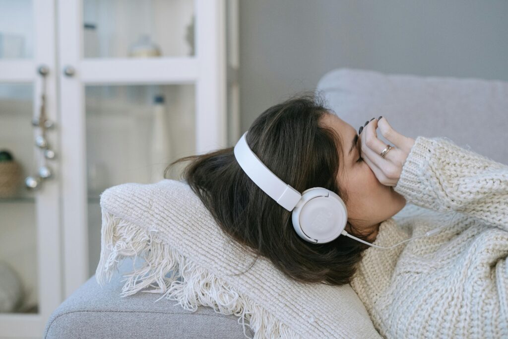 Woman lying on couch with headphones, appearing relaxed or contemplative indoors, cozy atmosphere.