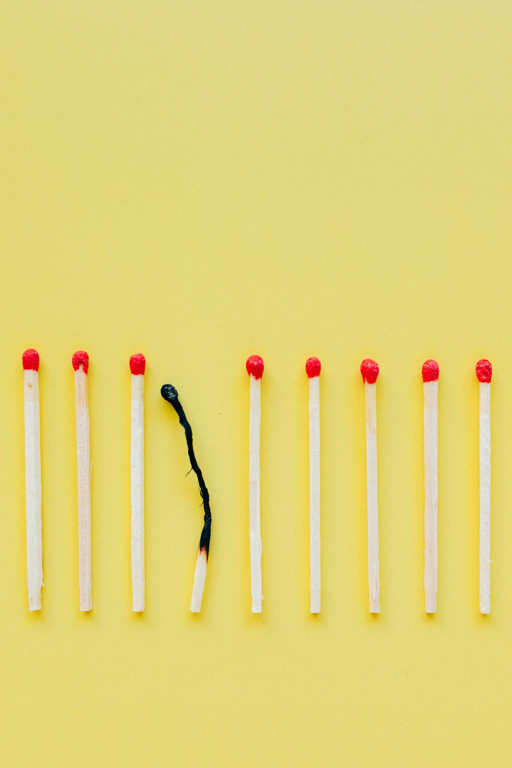 A line of matchsticks with one burned out symbolizes burnout and exhaustion against a yellow background.
